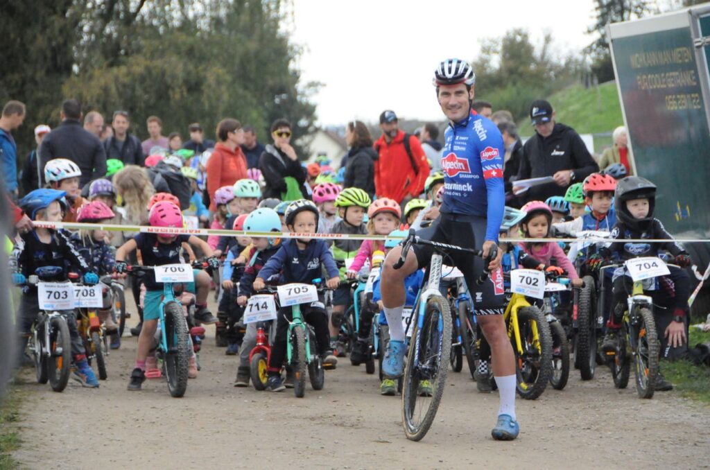 Rad-Profi Silvan Dillier sitzt auf dem Velo. Hinter ihm warten duzende Kinder auf den Rennstart.