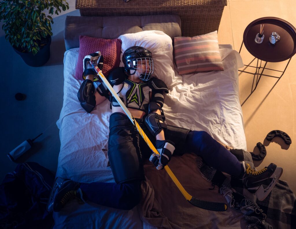 Ein Eishockeyspieler liegt mit seiner Ausrüstung im Bett.