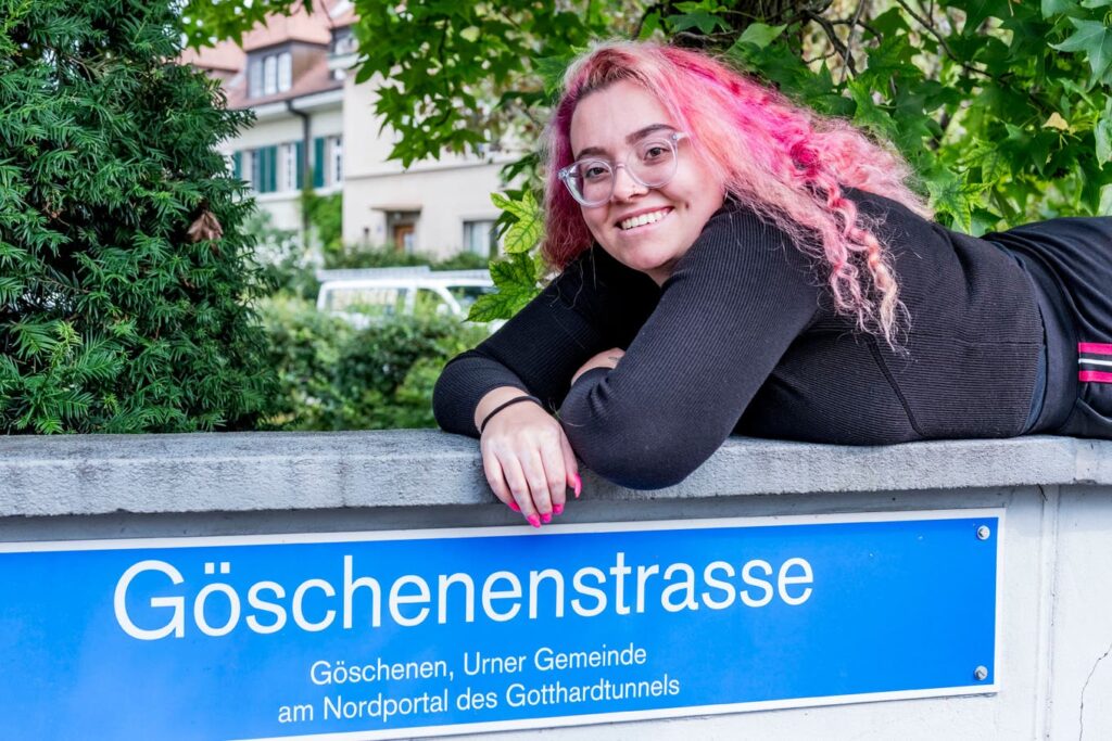 Frau mit pinken Haaren posiert mit dem Strassenschild der Göschenenstrasse in Basel.